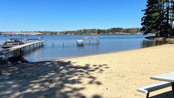 A lakeside beach with a dock, benches, and a picnic table.