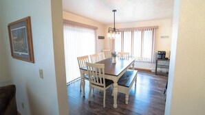 A dining area with a wooden table and white chairs, a chandelier, and a coffee machine.