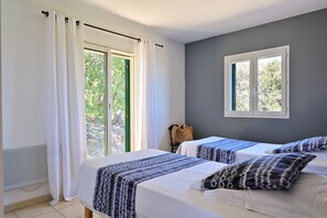 A hotel room with two beds, a large window with curtains, a view of greenery outside, and a small table with a bag. - Domaine Punta Della Guardia LE Calme ET LE Belvedere Sont LE Luxe vue mer (Cervione)