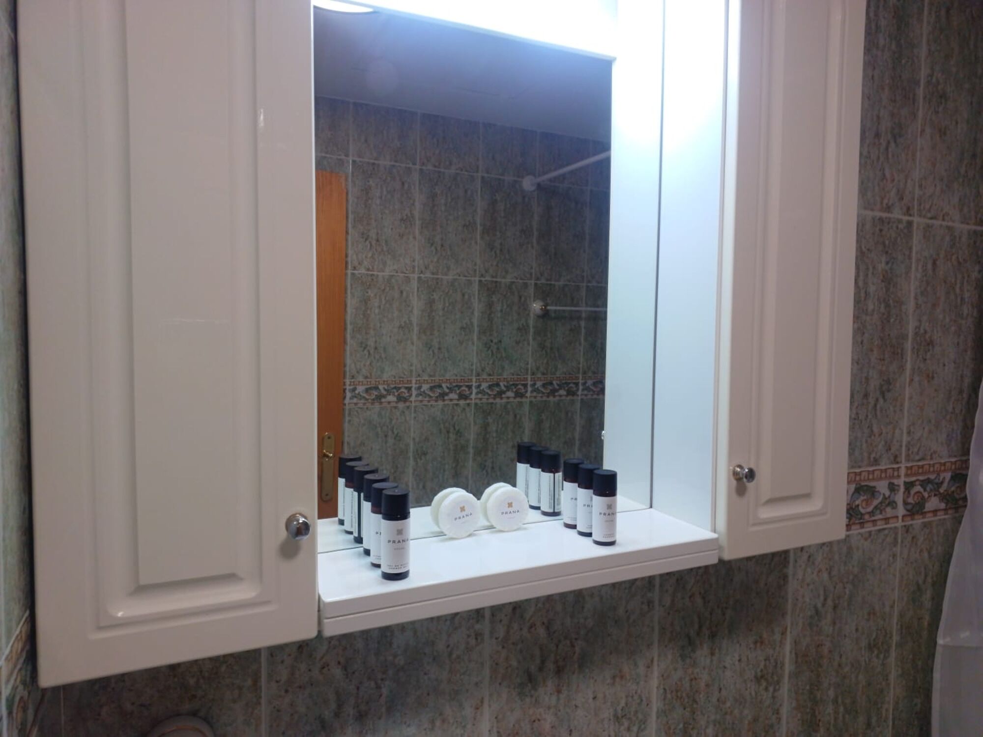 A bathroom with a vanity mirror, a shower, and a shelf with toiletries.