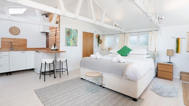 Un dormitorio moderno con una cama grande, un escritorio con dos sillas, una mesita redonda y un baño visible a través de una puerta abierta.
