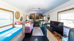A compact RV interior with a kitchenette, a seating area with a sofa and a table, and a television. - The Pinnacle Mountain Bus Stop ~ Fire pit, Frisbee Golf, Baggo, Hammock (Little Rock)