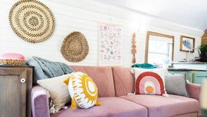 A cozy living room with a pink sofa, decorative pillows, and woven wall hangings. - The Pinnacle Mountain Bus Stop ~ Fire pit, Frisbee Golf, Baggo, Hammock (Little Rock)