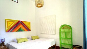 A room with a bed, a hanging light fixture, a colorful wall art piece, and a green chair. - Naupamanta Pacha (Chazuta)