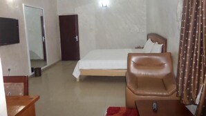 A hotel room with a bed, a chair, a TV, and a door. - Chinox Guest Inn (Abuja)