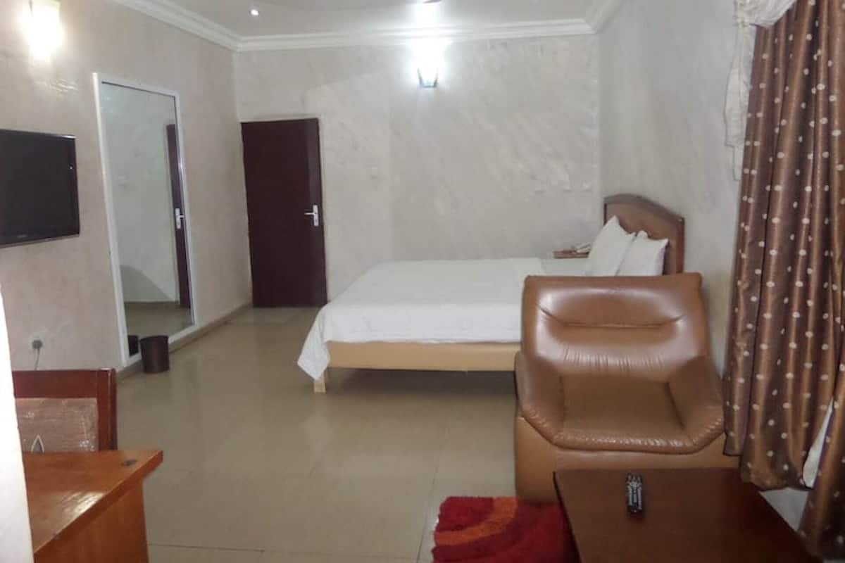 A hotel room with a bed, a chair, a TV, and a door.