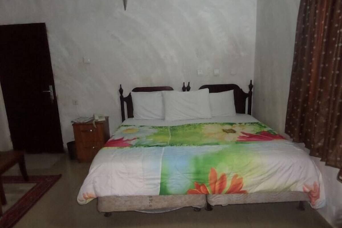 A single bed with a floral bedspread, a wooden headboard, and a nightstand with a telephone.