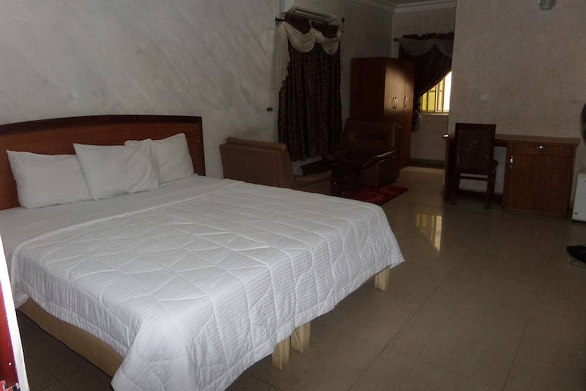 A hotel room with a large bed, a desk, and a chair.