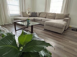 A living room with a glass coffee table, a beige sectional sofa, and large green plants. - Fabulous 2-bedroom condo in Arlington with WiFi access (Arlington)