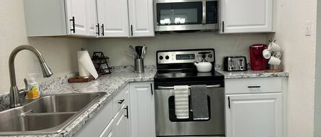 A modern kitchen with white cabinets, stainless steel appliances, a granite countertop, and a wooden floor.