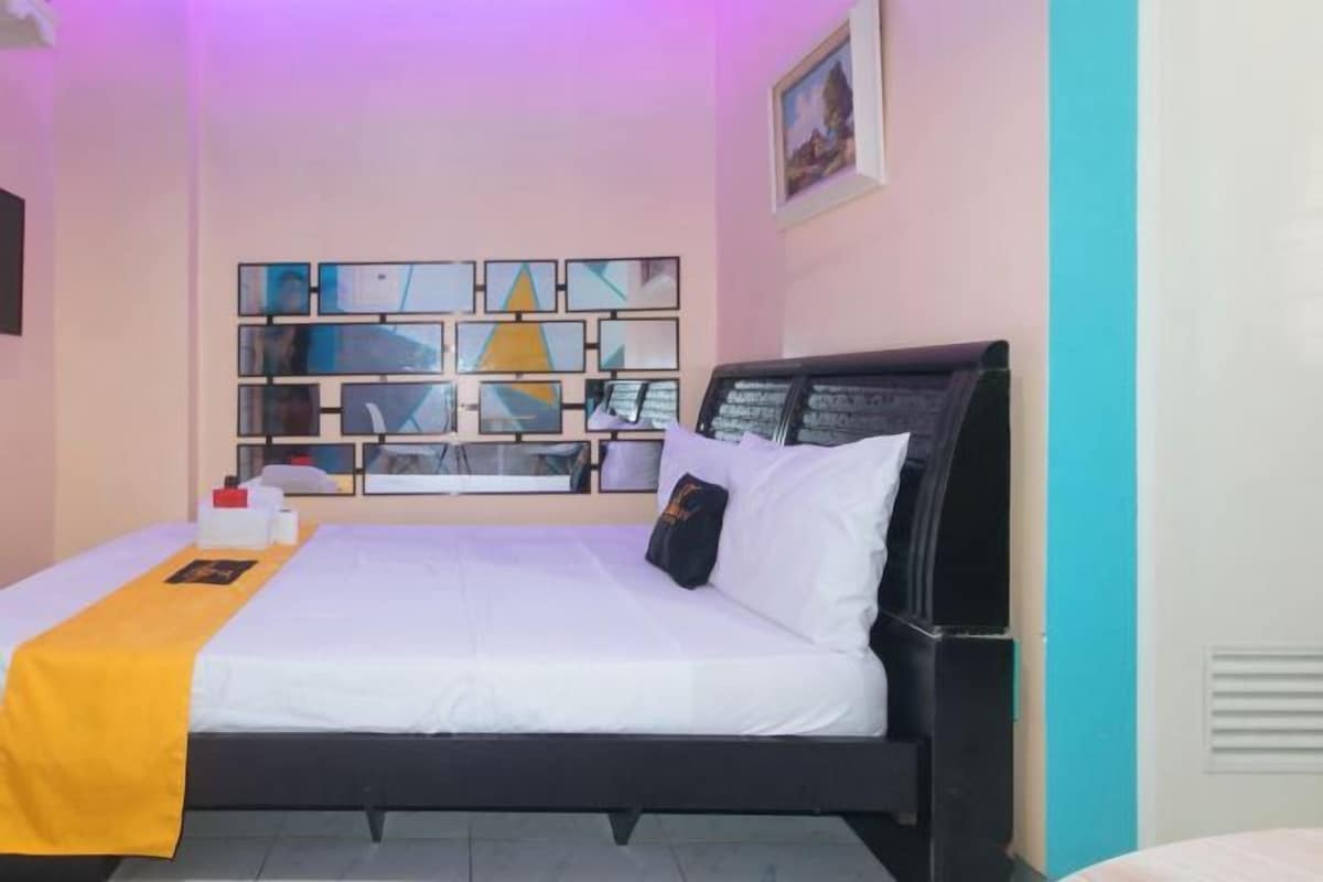 A hotel room with a bed, a bedside table, a wall-mounted TV, and a wall art display.