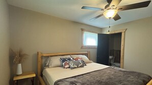 Een slaapkamer met een houten bed, een plafondventilator, een klein raam en een deur naar een badkamer.