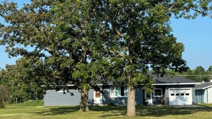 Een huis met een grote boom ervoor, een garage en een verzorgd gazon.