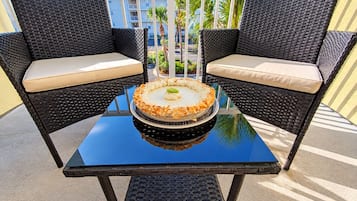 Duas cadeiras de vime com almofadas bege sobre uma mesa de vidro com uma sobremesa.