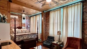 A room with a wooden ceiling, a ceiling fan, a bed with a headboard, a sofa, a chair, a table, and curtains. - Room 7 (sleeps 2) at Chipley's Squareview Inn (Carthage)