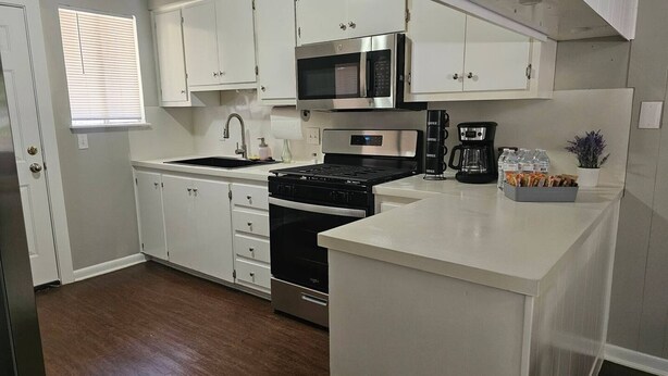 A kitchen with white cabinets, a stainless steel stove, a microwave, and a coffee maker. - Welcome to our inviting 2-bedroom home, perfect for accommodating up to 6 guests. Located just minutes from the Airport and McKinney Falls, this triplex-style home offers a comfortable stay with a private entrance. (Austin)