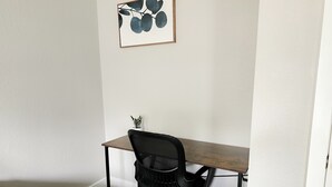 Un angolo di lavoro piccolo e ordinato, con scrivania, sedia e una cornice appesa al muro.