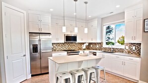 Una cocina moderna con armarios blancos, un refrigerador de acero inoxidable, un microondas y una isla grande con taburetes de bar.