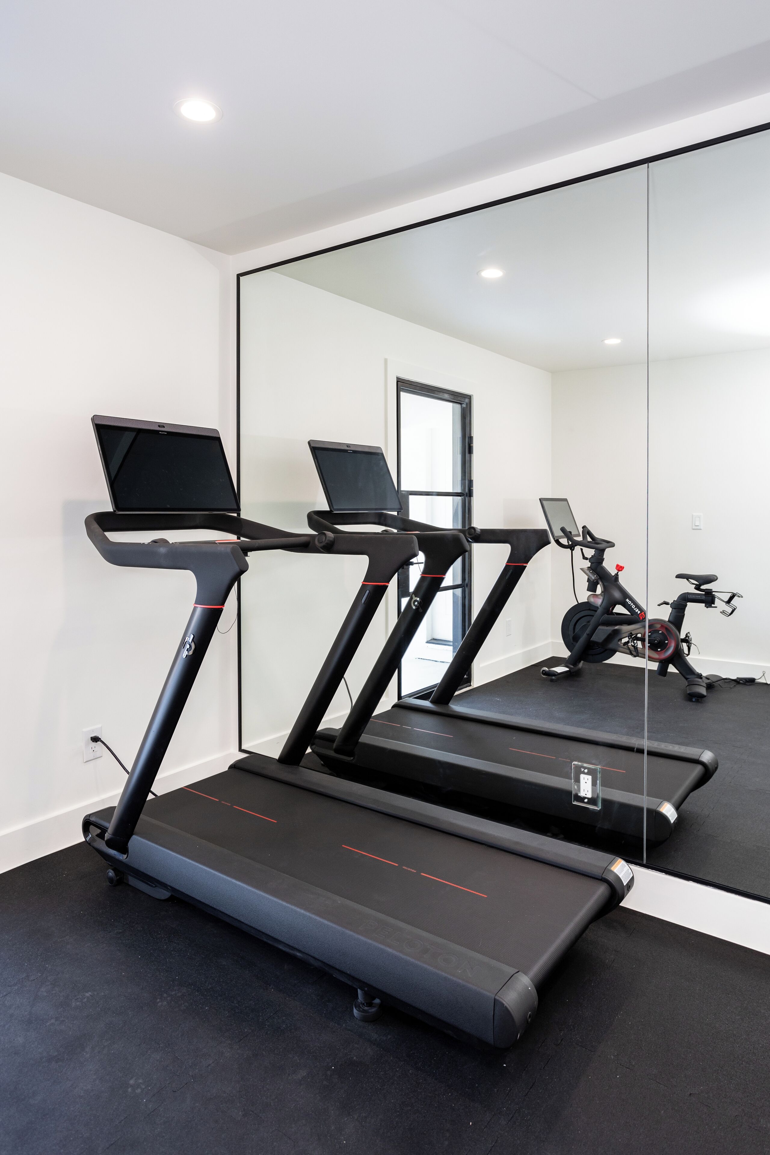 A home gym with three treadmills, a stationary bike, and a laptop on one treadmill.