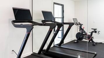 A home gym with three treadmills, a stationary bike, and a laptop on one treadmill.