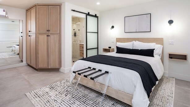 A modern bedroom with a large bed, a wardrobe, a sliding door, and a bedside table.