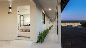 A hotel entrance with a covered walkway, a visible room with a bed and a suitcase, and a parking lot. - Hotel Bayit Modesto Salida (Salida)