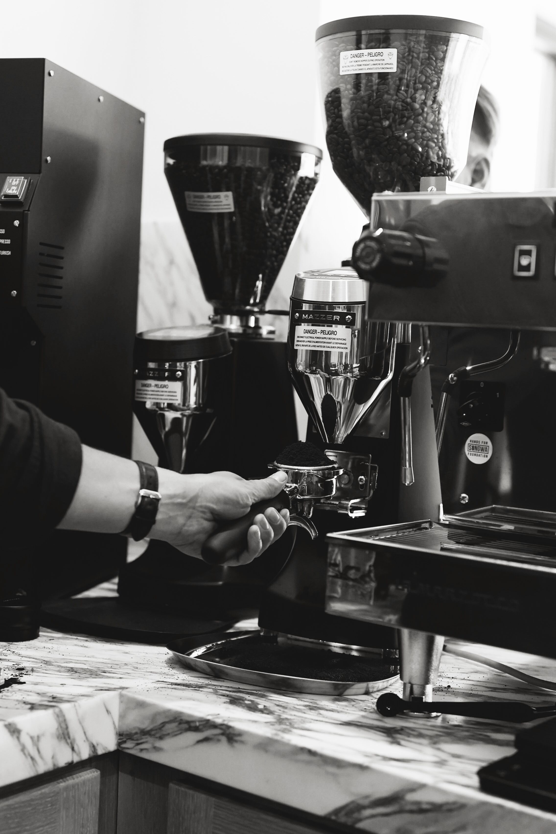 Une machine à café dotée d’un moulin et d’un porte-filtre, un plan de travail en marbre et une main tenant une tasse.
