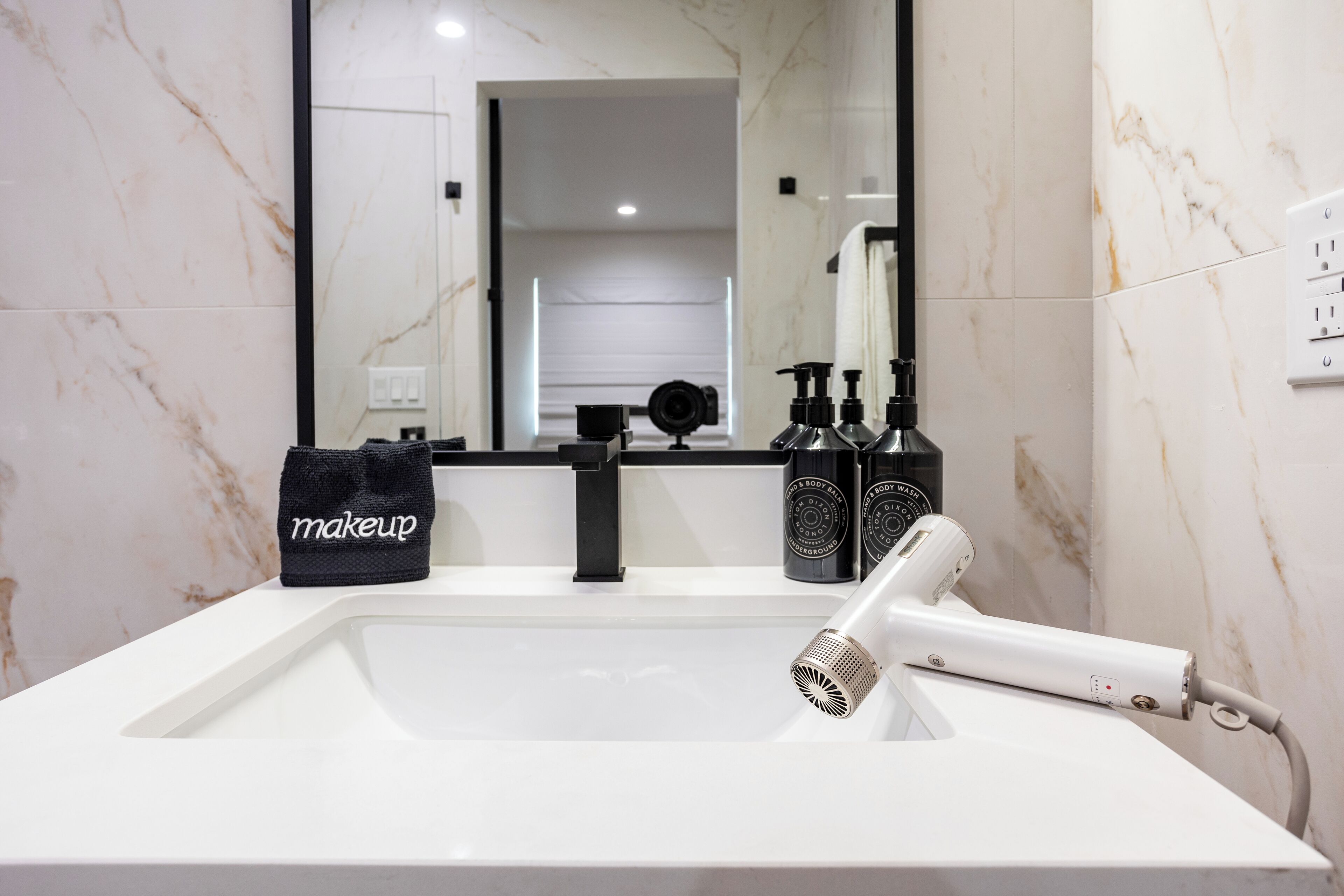 A bathroom with a white sink, a large mirror, and a hairdryer. There are bottles of shampoo and conditioner on the counter.
