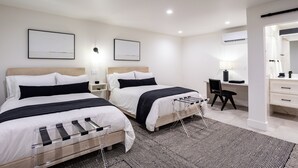 A hotel room with two beds, a desk, and a chair. There are two bedside tables with lamps.