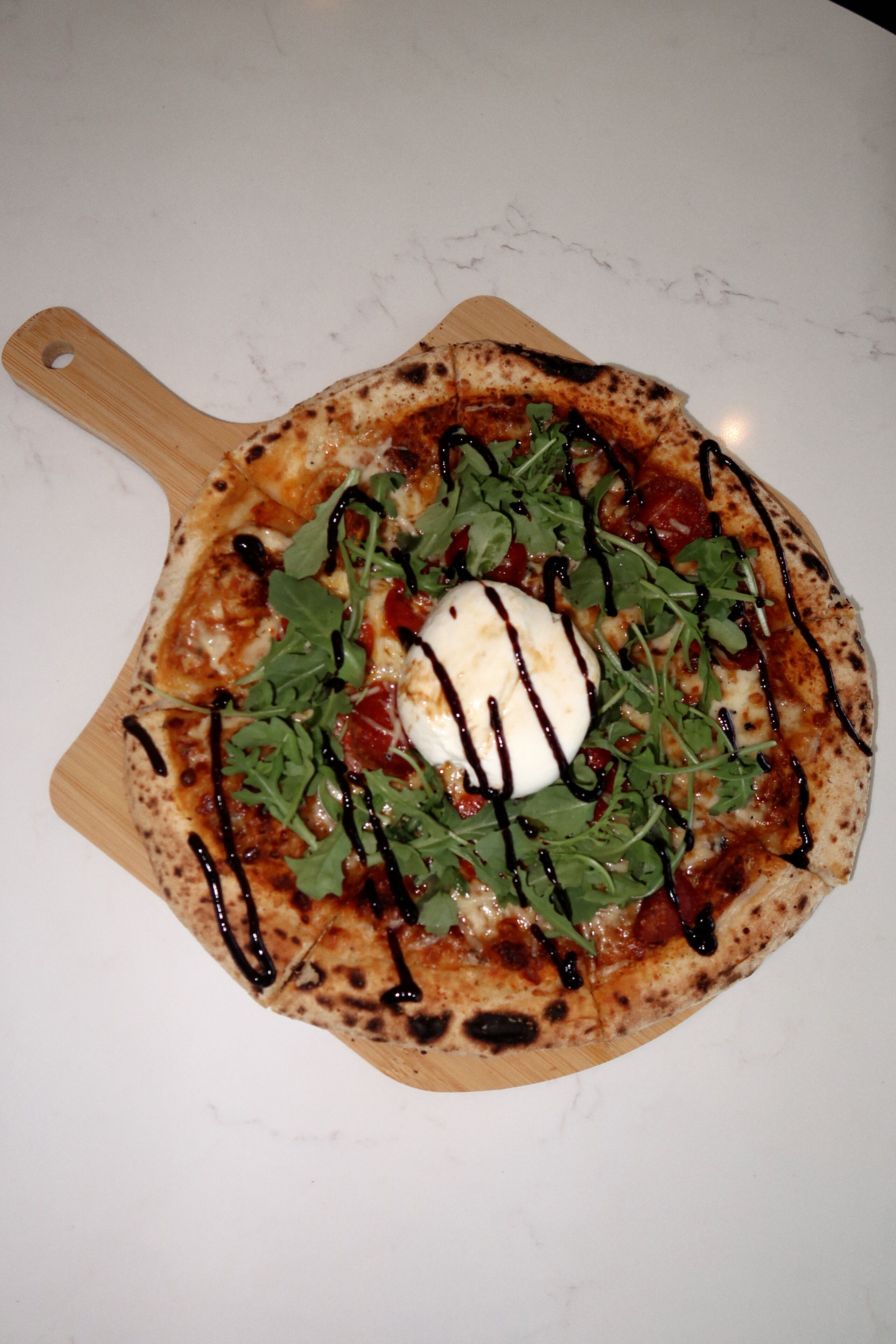 A pizza with greens and a white topping on a wooden board.