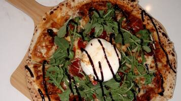 A pizza with greens and a white topping on a wooden board.