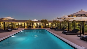 A swimming pool with lounge chairs and umbrellas, surrounded by a fence and trees. - Hotel Bayit Modesto Salida (Salida)