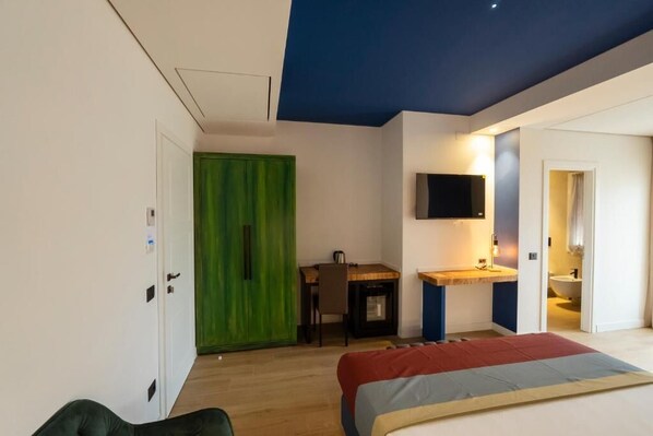 A bedroom with a bed, a desk, a TV, and a bathroom visible through an open door.