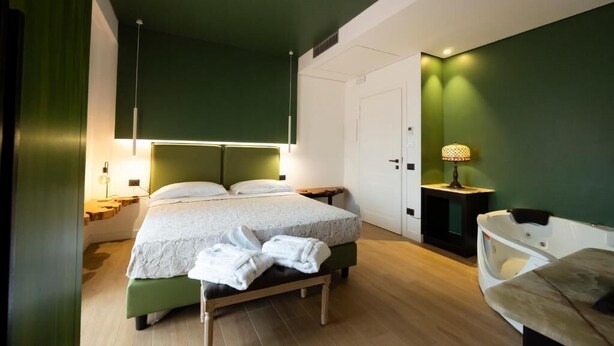 Een moderne hotelkamer met een bed, nachtkastjes, een bankje, een lamp en een zithoekje.