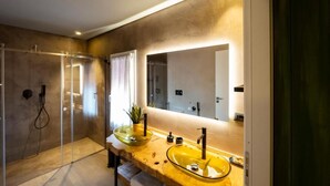 Een moderne badkamer met een douche met glazen wand, twee wastafels met een grote spiegel erboven en een potplant op het aanrecht.