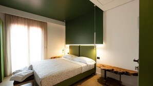 Een slaapkamer met een bed, nachtkastje, hanglamp en een raam met gordijnen.