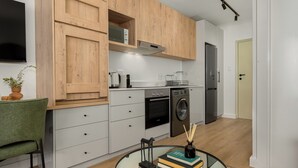 A modern kitchen with wooden cabinets, a built-in oven, a washing machine, and a glass table with books and a vase. - The Sage l Designer Studio l Balcony Views (Cape Town)