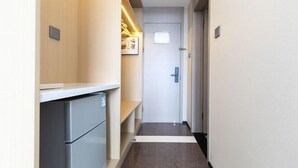 En smal hall med ett kylskåp, en dörr och en hylla med diverse föremål.