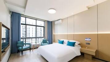 A hotel room with a large bed, a desk, a chair, a TV, and a window with curtains.