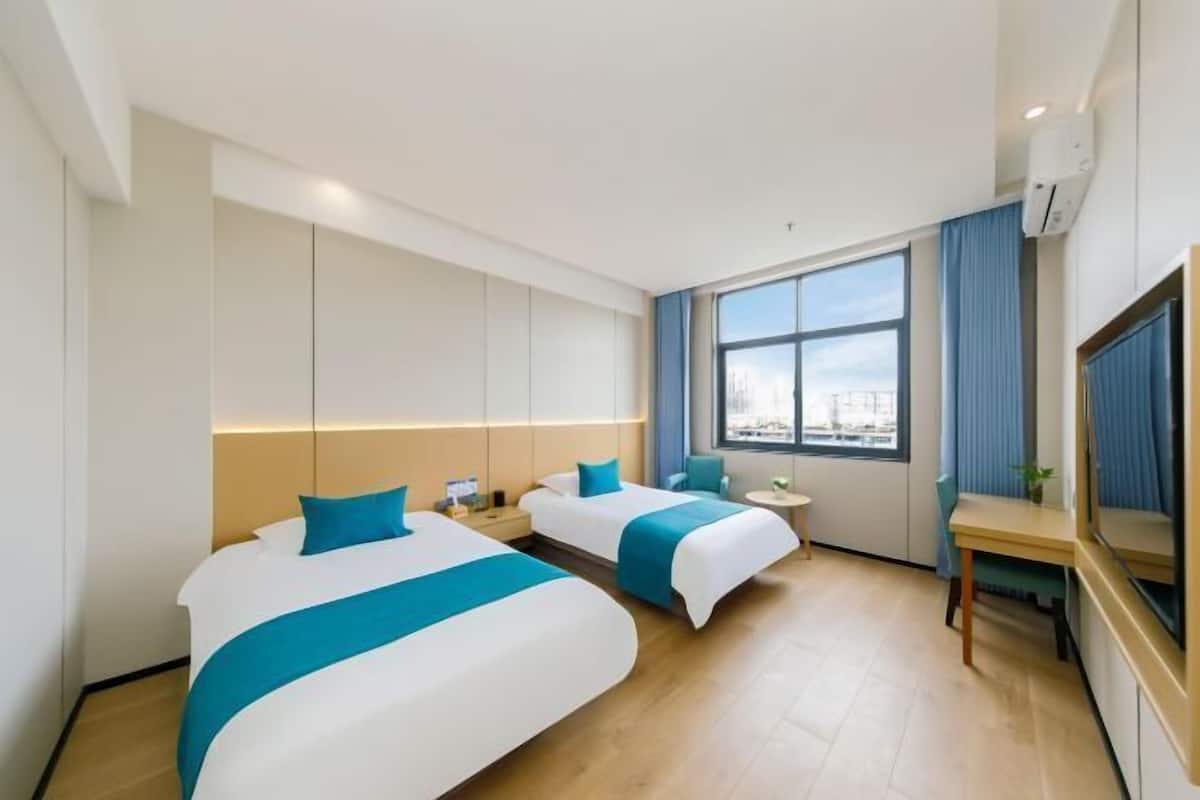 Camera d'albergo con due letti, una scrivania, una sedia, una televisione, una finestra con tende e un condizionatore d'aria.