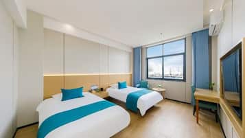 A hotel room with two beds, a desk, a chair, a TV, a window with curtains, and an air conditioning unit.