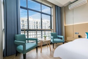 Une chambre d’hôtel avec une grande fenêtre, deux chaises, une petite table, un lit et un appareil de climatisation.