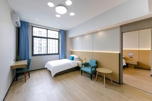 Habitación de hotel con cama, escritorio, silla, una mesita y ventana con cortinas.