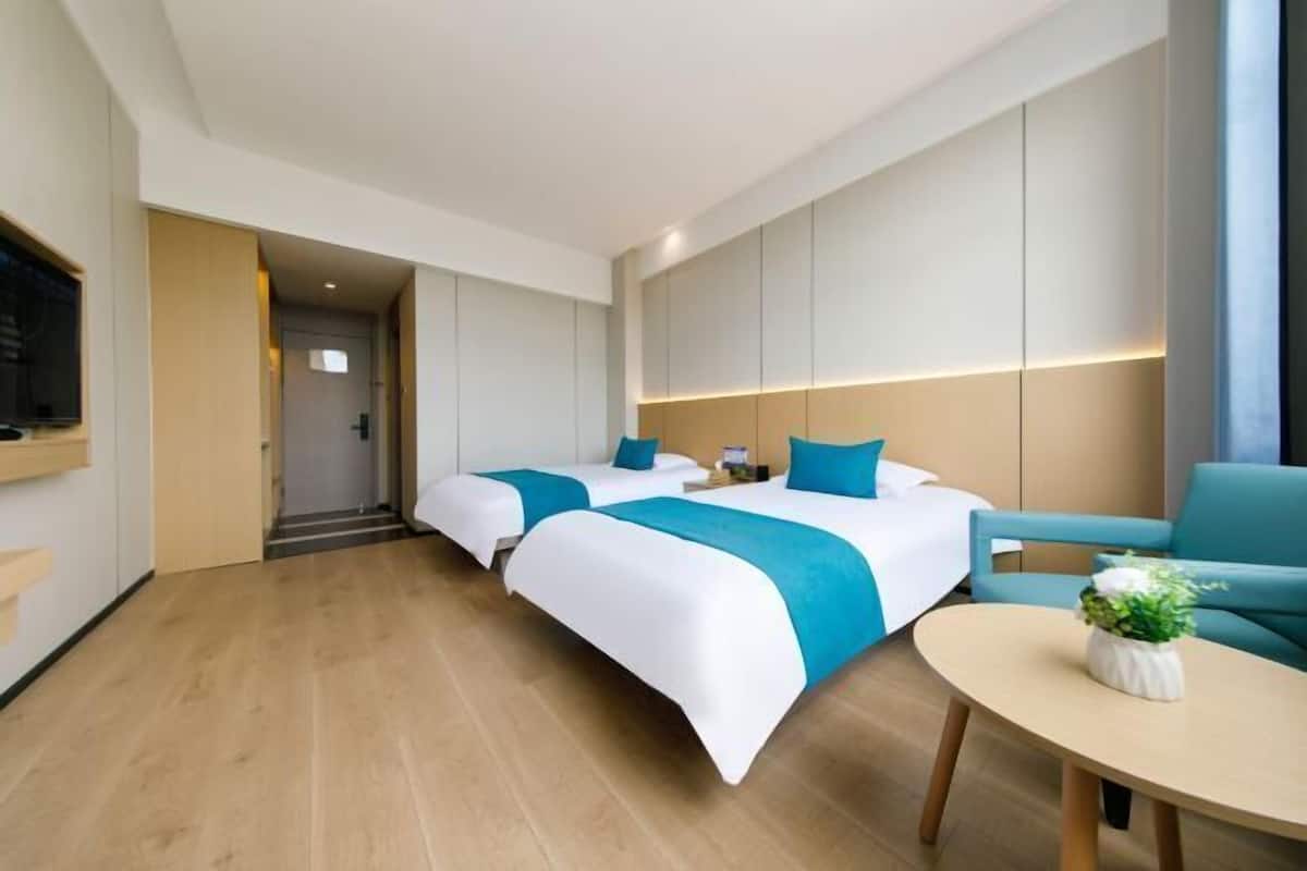 Camera d'albergo con due letti, un divano, un tavolo rotondo e una televisione.