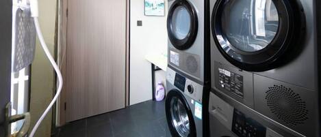 A laundry room with stacked washing machines and dryers, a door, and a wall-mounted control panel.
