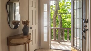 A hallway with a wooden console table, a mirror, and a rug leading to a glass door with a view of trees.