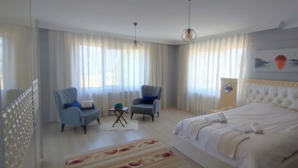 A modern hotel room with a large bed, two armchairs, a small table, and a view of the sea through the windows. - AKKAYALAR AERIE HOUSE (Bolu)