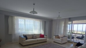 A spacious living room with a large window, a sofa, a chair, and a small table. - AKKAYALAR AERIE HOUSE (Bolu)