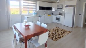 A modern kitchen with white cabinets, a dining table with chairs, and a view of the outdoors through large windows. - AKKAYALAR AERIE HOUSE (Bolu)