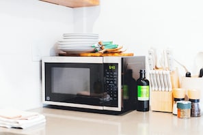 Una cucina con forno a microonde, una pila di piatti, una bottiglia d'olio d'oliva e un portachinelle.